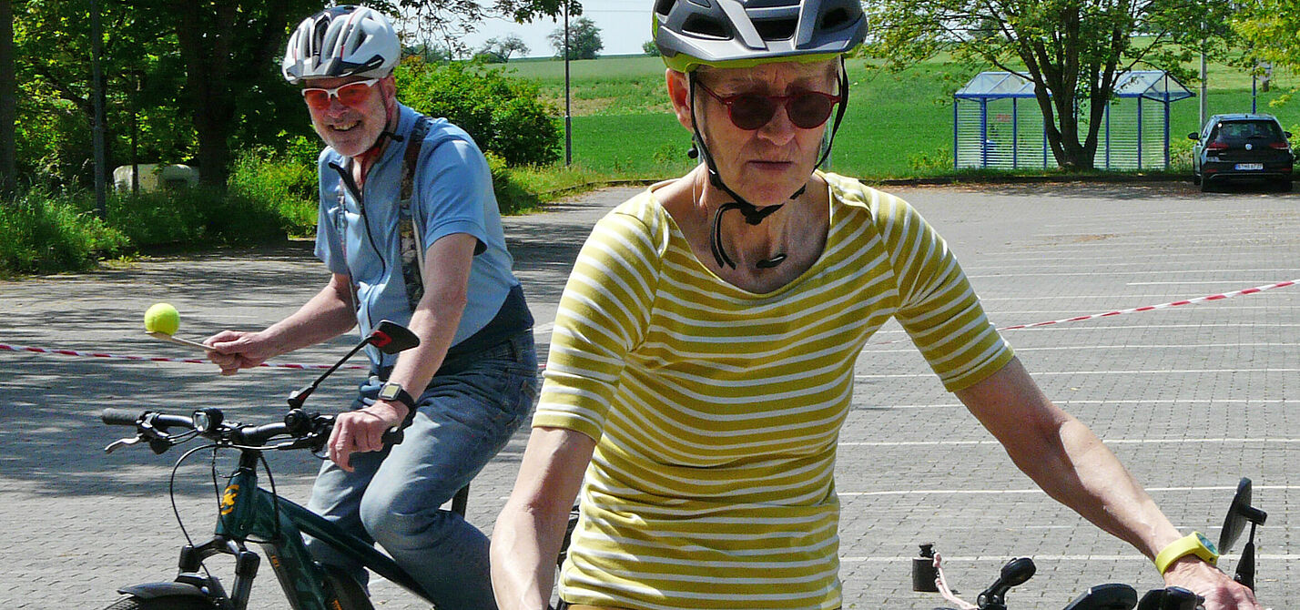 Zwei Radfahrende balancieren mit Bällen