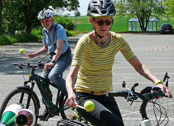 Zwei Radfahrende balancieren mit Bällen